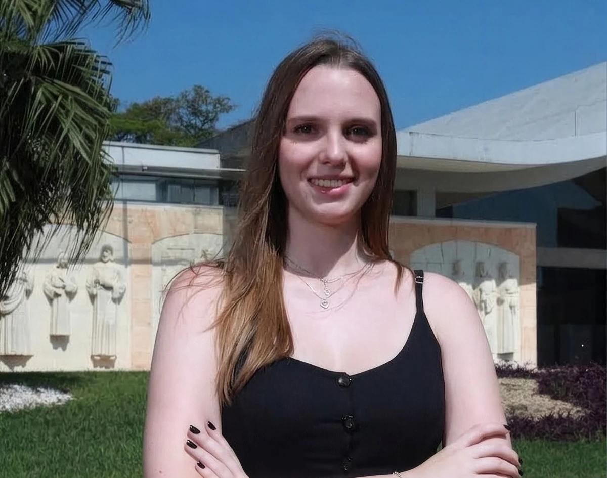 Gabriela Stellato sorrindo, de braços cruzados, em frente a um prédio
