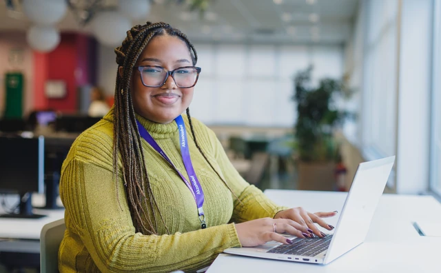Estagiária sorrindo enquanto trabalha no notebook