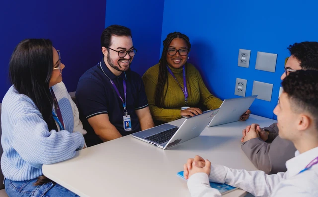 Grupo diverso de estagiários conversando em volta de uma mesa de reunião