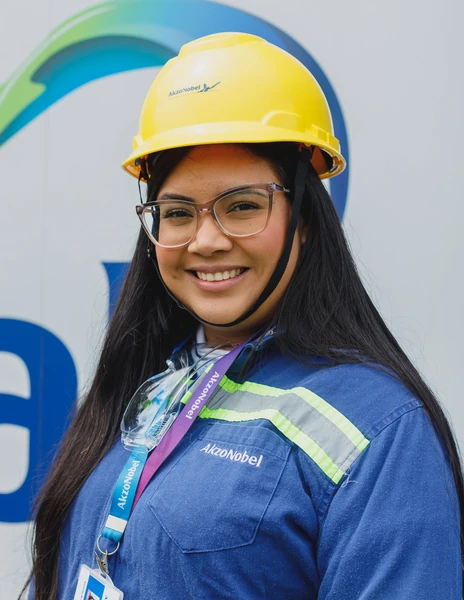 Colaboradora da AkzoNobel sorrindo, de capacete amarelo e uniforme azul